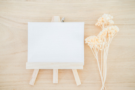 White canvas art board on wood texture background with dried flowerの写真素材