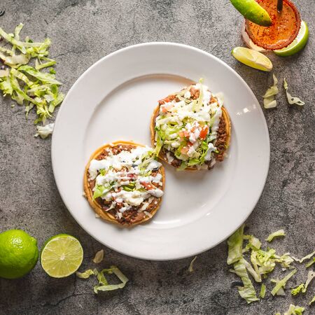 Beautifully plated and composed mexican taco plate with beans lettuce lime drink on grey gray surface from aboveの写真素材