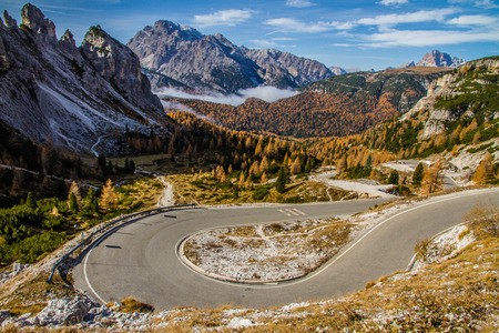 Winding road within Colorful Autumn Forest, Cloudy Blue Sky and Mountains-Dolomites,Italyの写真素材