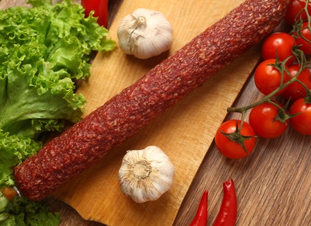 Salami sausage on a cutting board surrounded with various vegetables