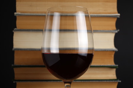 Glass of red wine on a reflective surface with booksの写真素材