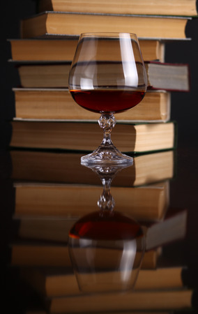 Glass of brandy on a reflective surface with booksの写真素材