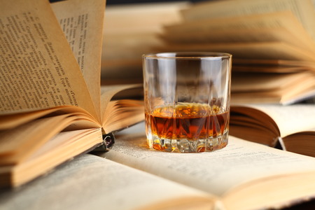 Glass of whiskey standing on several open booksの写真素材