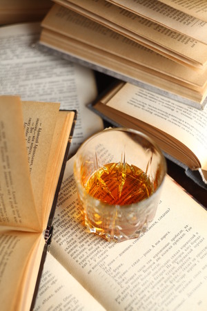 Glass of whiskey standing on several open booksの写真素材
