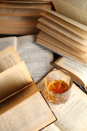 Glass of whiskey standing on several open booksの写真素材