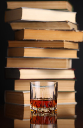 Glass of whiskey on a reflective surface with booksの写真素材