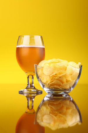 Glass of light beer with snacks over a bright yellow backgroundの写真素材