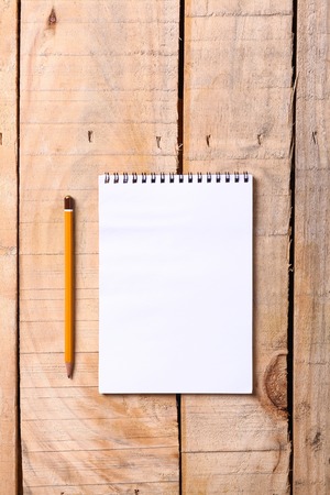 Blank white notepad with pencil on a grunge wooden surfaceの写真素材