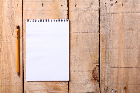 Blank white notepad with pencil on a grunge wooden surfaceの写真素材
