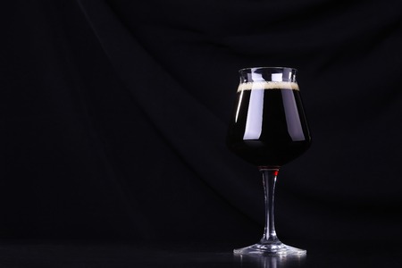 Glass full of dark beer over a black fabric background