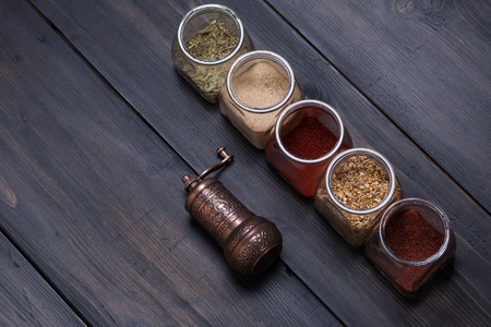 Several spice jars with spices and a small spice grinder on a dark wood surfaceの写真素材
