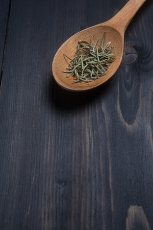 Wooden spoon with dried rosemary spice on a dark wooden surfaceの写真素材