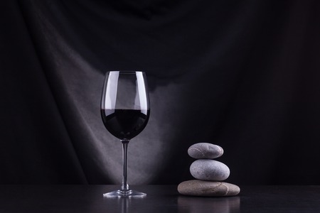 Glass of red wine on a dark table with a pile of stones nearbyの写真素材
