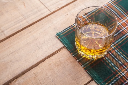 Glass of Scotch whisky on a traditional tartan cloth on a wooden tableの写真素材