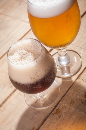 Small glass of dark beer and larger glass of light beer on a wooden tableの写真素材