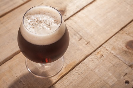Small glass of dark beer on a textured wooden tableの写真素材
