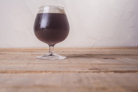 Small glass of dark beer on a textured wooden tableの写真素材