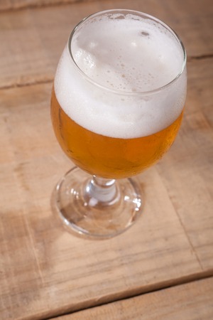 Glass of light beer with tall white foam head on a wooden table
