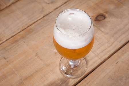 Glass of light beer with tall white foam head on a wooden tableの写真素材