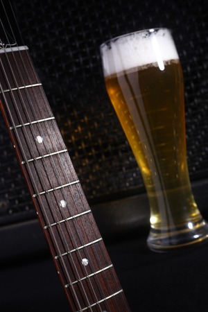 Tall glass full of light beer standing near a grilled music monitor with a guitar fretboard in the foregroundの写真素材