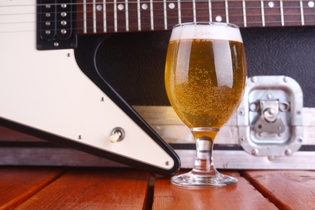 Glass full of light beer standing on a wooden table with a music equipment case and electric guitar...