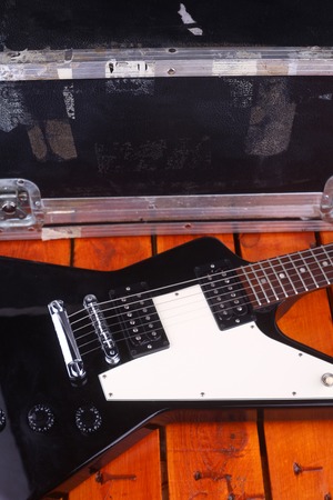 Closeup of an electric guitar body on a wooden surface with equipment case in the background