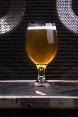 Glass full of light beer standing on a music equipment crate near a big grilled music monitorの写真素材