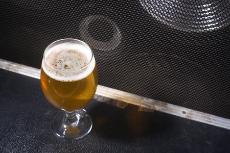 Glass full of light beer standing on a music equipment crate near a big grilled music monitor