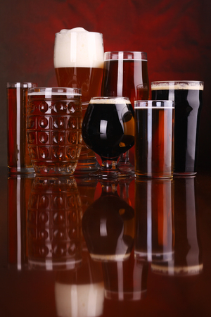 An assortment of various beer glass shapes and styles on a wooden table with a drapery in the backgroundの写真素材