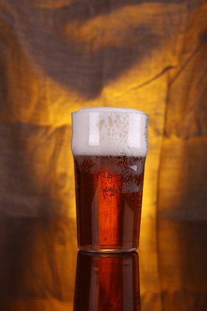 Nonic pint glass with light beer with a warm colored drapery in the backgroundの写真素材
