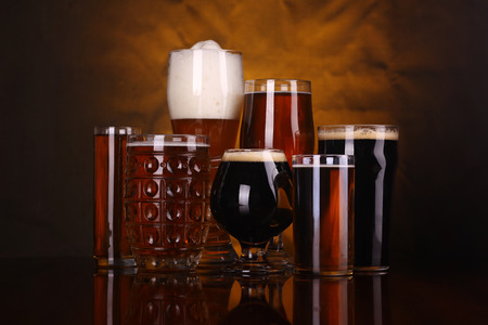 An assortment of various beer glass shapes and styles on a wooden table with a drapery in the backgroundの写真素材