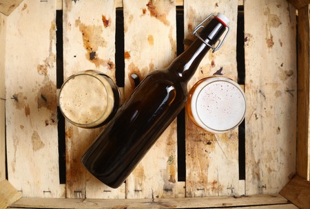 Bottle and full glasses of beer looking as a percent sign in a dirty wooden crateの写真素材