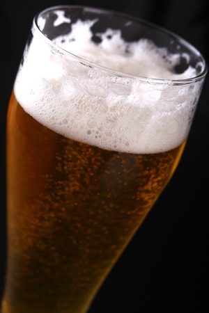 Tall glass of sparkling lager beer over a dark background