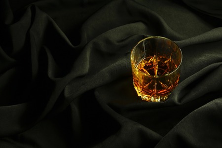 Tumbler glass of whiskey standing on black crumpled fabric