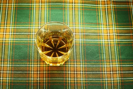 Glass of Skotch whiskey resting on a traditional tartan clothの写真素材
