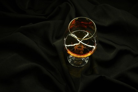 Glass of brandy standing on a crumpled black fabric