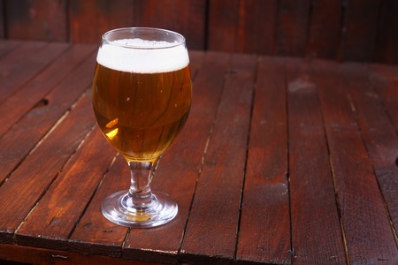 Glass full of light beer standing on a wooden table