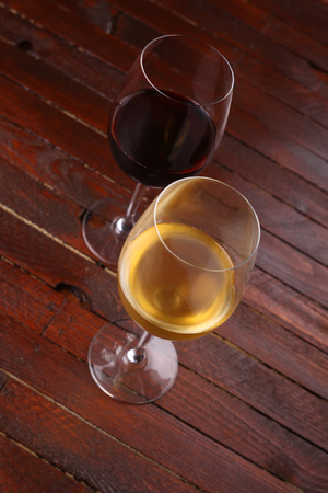 Two tall glasses with red and white wine standing on a wooden tableの写真素材