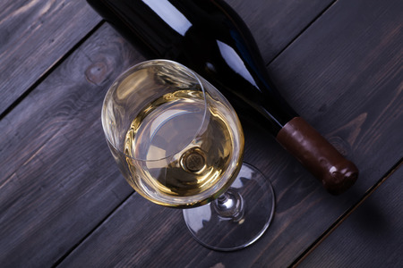 Bottle and glass of white wine on a textured dark wood surfaceの写真素材