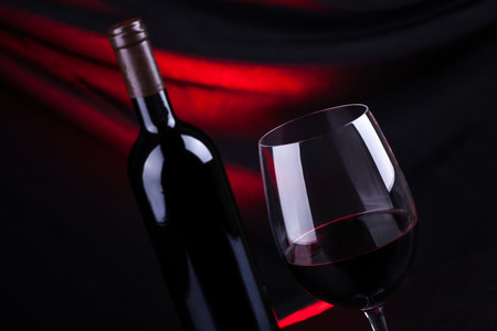 Glass and bottle of red wine with a dark background lit by a red lightの写真素材