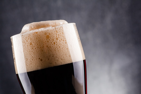 Tall glass of dark beer over a dark textured wooden backgroundの写真素材