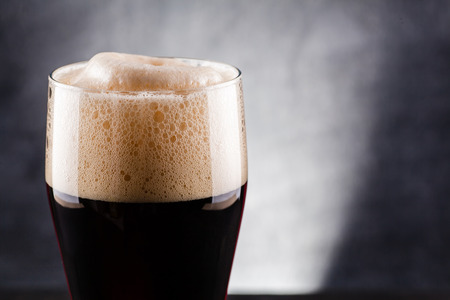 Tall glass of dark beer over a dark textured wooden background