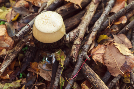Glass full of dark beer on the forest floor among leaves and branches on an autumn day