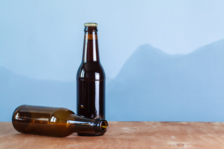 Full and empty beer bottles with no label on a wooden surface over an abstract blue background