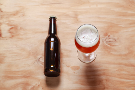 Glass full of amber beer and a beer bottle on a textured wooden surface