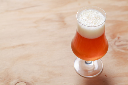 Glass of amber beer on a textured wooden surfaceの写真素材