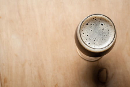 Glass full of dark  beer on a textured wooden table