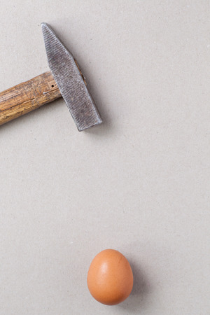 A big hammer hovering above a fragile raw chicken egg over a light gray backgroundの写真素材