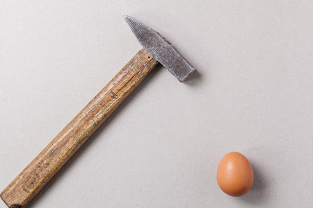A big hammer hovering above a fragile raw chicken egg over a light gray backgroundの写真素材