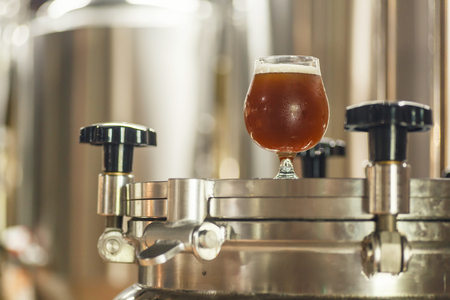 Glass full of amber ale beer standing on equipment at a breweryの写真素材